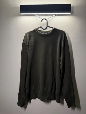 Olivegrön sweatshirt - En enkel och stilren olivgrön sweatshirt med rund halsringning och långa ärmar. Tröjan har ribbade muddar vid ärmslut och nederkant, perfekt för en avslappnad och clean look. Passar till det mesta och är lätt att matcha.