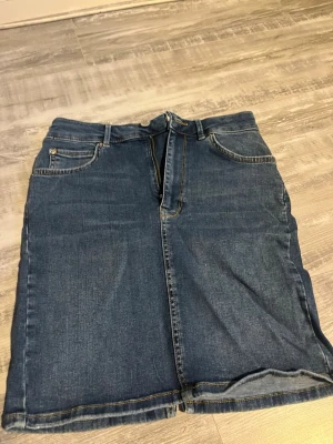 Blå jeanskjol från gina tricot - Klassisk blå jeanskjol från gina tricot med fem fickor, bälteshällor och dragkedja framtill. Kjolen har en rak passform och är tillverkad i slitstarkt bomullsmaterial. Perfekt att matcha med sneakers eller boots för en avslappnad look.