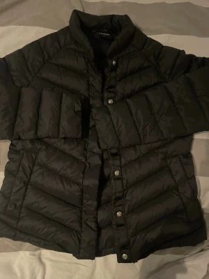 Svart vårjacka från Everest - Snygg svart vindjacka från Everest med quiltad design och tryckknappar framtill. Jackan har hög krage och raka ärmar. Liten i storlek