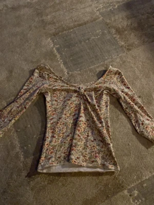 Blommig långärmad topp med rosett - Supersöt långkortärmad topp med blommigt mönster i pastelliga färger och liten rosett framtill. Toppen har en lätt v-ringad urringning och är figurnära i modellen. Perfekt att styla med jeans eller kjol för en trendig look. Knappt använd 1 gång💕💕🫰🏼🫰🏼