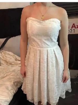 Perfekta spets studentklänning❤️ - Axelbandslös vit klänning med spetsmaterial och kort längd. Klänningen har en dragkedja i ryggen och ett fint fall med veckad kjol. Perfekt för dig som vill ha en elegant och stilren look. Byggel inbygd. För referens är jag 1.57 och xs/s☺️