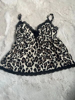 Leopardmönstrat linne Gina Tricot - Snyggt leopardmönstrat linne från Gina Tricot med tunna, justerbara axelband och svart spetskant vid urringningen och nederkanten. Materialet är glansigt och mjukt. Djurmönstret ger en trendig vibe.