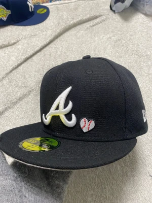 Svart New Era 59FIFTY keps 7 3/8 - Säljer en svart New Era 59FIFTY keps från Cooperstown Collection. Kepsen har broderad text 'LOVE & HUSTLE = GAME' i vitt och rött samt en gul brodyr på sidan. Skärmen är grå undertill och materialet är 100% polyester.