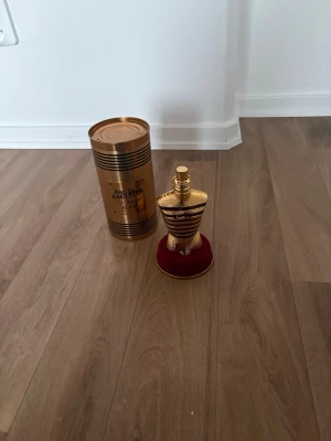 Jean Paul Gaultier elixir 125ml - Lyxig parfym från Jean Paul Gaultier i den ikoniska guldformade flaskan som liknar en kvinnokropp. Kommer med originalförpackning i metall, också i guld. Doften är elegant och flaskan står på en röd sammetsliknande bas. Perfekt för dig som gillar exklusiva parfymer.