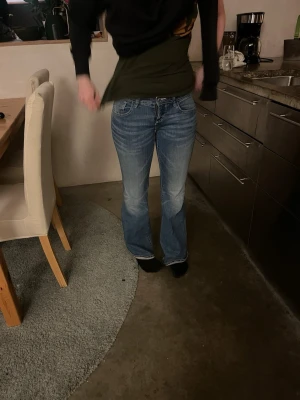 Blå bootcut jeans med slitningar - Säljer ett par blå bootcut jeans med råsa sömmar och ljusare partier framtill. Jeansen har klassisk femficksdesign och låg midja.