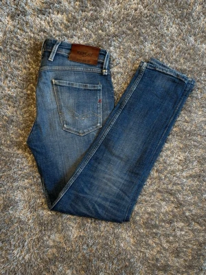 Replay jeans - Snygga blå jeans från Replay i modell Anbass vilket är slim. Med klassisk femficksdesign och lätt slitna detaljer framtill. Jeansen har en schysst tvätt med diskreta slitningar och är tillverkade denim för en bekväm och tålig känsla. Perfekta för en trendig och avslappnad stil. Storlek W29 & L30