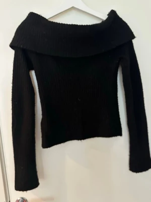 Svart off shoulder stickad tröja - Säljer en svart ribbstickad tröja med bred off shoulder-krage och långa ärmar. Tröjan har en figurnära passform. Materialet känns mjukt och stretchigt.