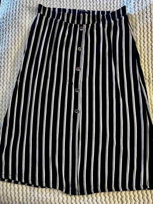 Svartvitrandig midikjol med knappar 🌟 - Säljer en jätteskön svart- & vitrandig midikjol från mywear woman! 🤍 Snygg resår i midjan, träknappar och slits fram. Luftigt och snyggt a-linjeformat fall, perfekt för sommaren. Mått: Midja tvärsöver ca 37 cm (resår), längd 76 cm, vidd nedtill 65 cm. Se bilder! Skick: Toppskick & sparsamt använd. Nypris ca 250 kr.  Gör gärna paketpris med mina andra plagg för billigare frakt! 📦✨