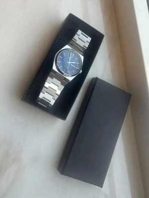 Silverfärgad klocka med blå urtavla - Stilren klocka med länkarmband i silverfärgad metall och blå urtavla. Klockan har minimalistisk design med tydliga markeringar och klassiskt spänne. Perfekt accessoar för dig som gillar en clean look.