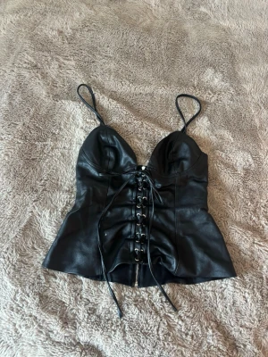 Svart korsettopp i skinnimitation - Snygg svart korsettopp från Zara i XS men funkar som XS-M pga snörningen. Toppen har en figurnära passform som framhäver midjan. Endast använd en gång så den har inga anmärkningar.🌟