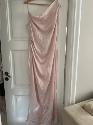 Ljusrosa långklänning från Adoore - Elegant ljusrosa långklänning från Adoore med tunna axelband och draperad front. Klänningen har en mjuk, glansig yta och subtilt blommönster. Perfekt för sommarens speciella tillfällen. Har en mindre lagning i sidsöm (se sista bild), inget som syns när klänningen bärs tack vare draperingen. Därav anpassat pris. Nypris ca 1 590 kr.