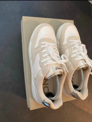 Vita och beige sneakers från Only - Snygga sneakers från Only i vitt och beige med klassisk låg profil. Skorna har vita snören, perforerad tå och detaljer i mocka samt metallic på hälen. Perfekta för dig som gillar stilrena och trendiga sneakers.