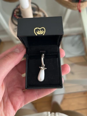 Maria Nilsdotter örhänge med pärldroppe - Säljer ett stilrent örhänge från Maria Black med en droppformad vit pärla hängande i en silverfärgad ring. Örhänget har en modern och minimalistisk design som passar perfekt till olika stilar.