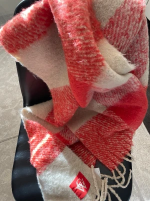 Rödvit halsduk från Carin Wester - Stor och fluffig halsduk från Carin Wester i röd- och vitrutigt mönster. Tillverkad i borstad polyester som känns mjuk och varm. Halsduken har fransar i ändarna och en snygg logotypetikett. Perfekt för att addera färg till din outfit.