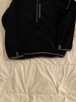 Svart fleece tröja med halv dragkedja.  - Mysig svart fleece tröja med halv dragkedja framtill och en bröstficka med dragkedja. Grå detaljer vid muddar och nederkant. Perfekt för lager-på-lager och chill dagar. Långärmad och enkel att matcha till det mesta.