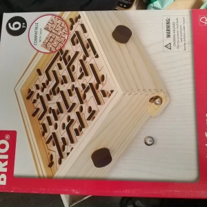 BRIO Labyrintspel i trä - Klassiskt labyrintspel från BRIO i ljust trä med svarta rattar på sidorna för att styra kulan genom banan. Spelplanen har numrerade hål och snirkliga gångar. Perfekt för dig som gillar utmanande och roliga spel.