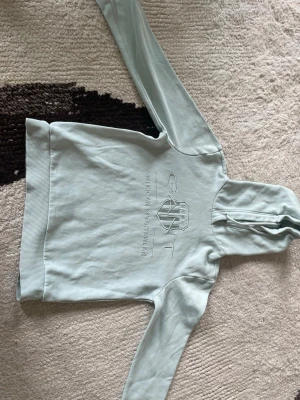 Ljusgrön hoodie från GANT - Snygg ljusgrön hoodie från GANT med broderad logga och text på bröstet. Klassisk modell med huva och ribbade muddar vid ärmslut och nederkant. Tillverkad i mjukt bomullsmaterial som känns skönt mot huden. Perfekt för en avslappnad och stilren look.