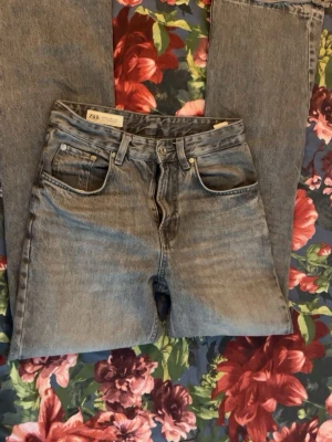 Grå raka jeans från Zara - Säljer ett par grå raka jeans från Zara med klassisk femficksmodell och hög midja. Jeansen har en snygg tvättad look och är tillverkade i bomull. Perfekta för en avslappnad och trendig stil.