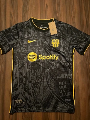 Barcelona Nike matchtröja svart/gul - Snygg FC Barcelona matchtröja från Nike i svart med gula detaljer och tryck. Tröjan har korta ärmar, klubbmärke och sponsorloggor på bröstet samt ett unikt mönster inspirerat av Barcelonas arkitektur. Tillverkad i lätt och ventilerande funktionsmaterial.