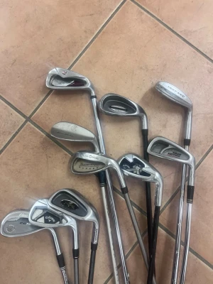 Set med golfklubbor i metall - Alla klubbor tillsammans för 3500kr men om du väljer en eller två så kan vi lösa upp ett pris.    Säljer ett blandat set golfklubbor från Callaway och TaylorMade och massa andra. Klubborna är i silverfärgad metall med svarta detaljer och olika modeller för varierat spel. Perfekt för dig som vill komplettera din golfutrustning eller testa olika klubbor. 