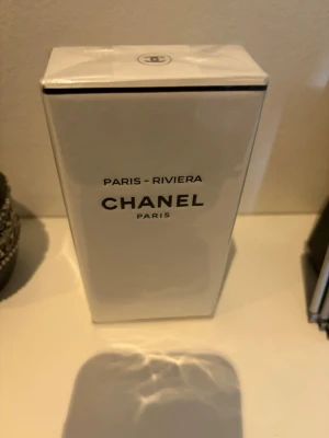 Chanel Paris-Riviera parfym - Exklusiv parfym från Chanel, Paris-Riviera, i elegant vit kartong med svart text. Förpackningen har en stilren och minimalistisk design som utstrålar lyx och klass. Perfekt för dig som gillar ikoniska dofter och snygga flaskor.