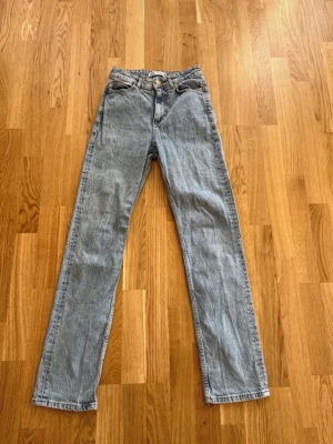 Blå raka jeans från Zara - Säljer ett par klassiska blå raka jeans från Zara med hög midja och fem fickor. Jeansen har en ljus tvätt och stängs med dragkedja och knapp. Perfekta för en avslappnad och trendig look.