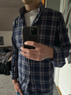 Blårutig skjorta  - Snygg blårutig skjorta med vita och röda detaljer. Skjortan har klassisk krage, långa ärmar och knäppning framtill. Perfekt för dig som gillar en avslappnad men ändå stilren look.