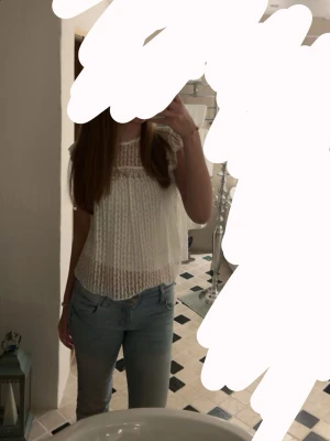 Vit spetsblus med volangärmar - Söt vit blus i spets med volangdetaljer på ärmarna och rund halsringning. Blusen är lätt transparent och har ett luftigt fall, perfekt till jeans eller kjol. Materialet är spets med fina mönster och blusen har en romantisk vibe.
