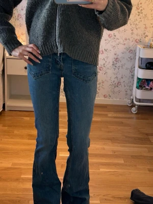 Blå bootcut jeans med fickdetaljer - Säljer ett par blå bootcut jeans med snygga fickdetaljer fram och bak. Jeansen har en klassisk blå tvätt och är tillverkade i denim med lätt stretch. Perfekta för dig som gillar en avslappnad men trendig look.
