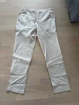 Beiga linnebyxor från Dressmann - Snygga beiga linnebyxor från Dressmann med dragsko i midjan och avslappnad passform.  Perfekta för en chill och stilren look. 