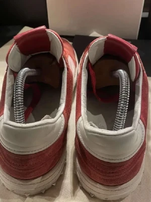 Röda och vita sneakers i mocka - Säljer ett par snygga flycrews som har nästan alla spikar kvar där bak men några är borta annars skulle jag inte säga att dom har något mer fel 