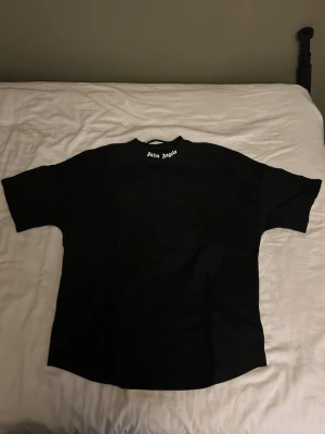Svart Palm Angels t-shirt med tryck - Svart t-shirt från Palm Angels med stort vitt logotryck på ryggen och mindre logga vid halsen. Klassisk passform med korta ärmar och rund hals. Perfekt för dig som gillar streetwear och vill sticka ut med en ikonisk design.