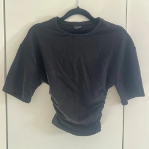 Svart topp - Säljer en svart  t-shirt med rund hals och korta ärmar som sitter åt i midjan. T-shirten har en enkel och stilren design, perfekt för att matcha med jeans eller kjol. Materialet känns mjukt och bekvämt mot huden. Endast testad. 