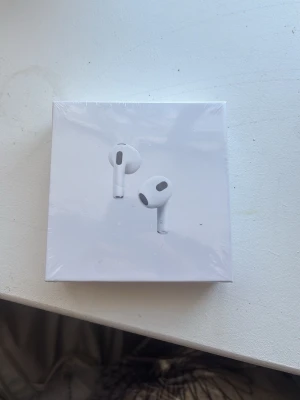 Apple AirPods med MagSafe-laddningsetui - Säljer ett par vita Apple AirPods med MagSafe-laddningsetui. Trådlösa in-ear hörlurar i stilren design, tillverkade i plast. Perfekta för musik, samtal och smidig anslutning till Apple-enheter. Levereras i originalförpackning. Inte öppnad kan öppnas och skicka bilder vid behov av köpare.
