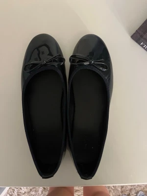 Svarta lackade ballerinaskor med rosett - Svarta ballerinaskor i glansigt lackmaterial. Ungefär storlek 39/40 och även aldrig använda💕