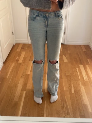 Ljusblå slitna jeans med hål - Säljer ett par ljusblå jeans med raka ben och stora hål vid knäna. Jeansen har klassisk femficksmodell och broderade detaljer på bakfickorna. Perfekta för en avslappnad och trendig look.