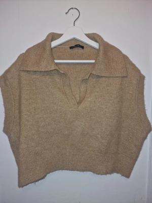Beige stickad väst med krage - Beige/brun stickad väst från Dilvin Chiquelle med bred krage och v-ringad öppning framtill. Perfekt att styla över en skjorta eller t-shirt för en trendig lager-på-lager-look. Använd och tvättad 1 gång.