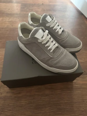 Grå sneakers från Brunello Cucinelli - Snygga grå sneakers från Brunello Cucinelli med vit sula och vita skosnören. Ovandelen är i mesh och mocka för en clean och exklusiv look. Perfekta för dig som gillar stilrena och lyxiga sneakers med premiumkänsla.