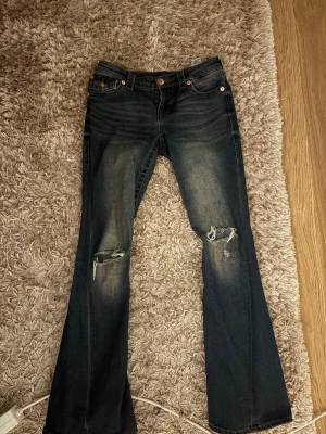 Mörkblå bootcut jeans med slitningar - Säljer ett par mörkblå bootcut jeans från True Religion med slitningar och hål på båda knäna. Low Waist och modellen ”joey” storlek 26🩷