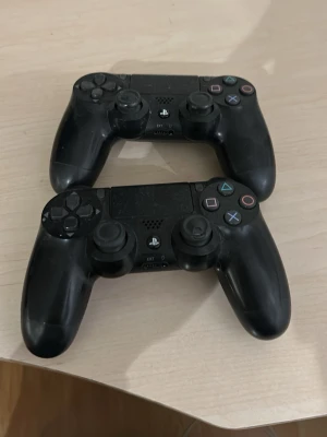 Svarta PS4 DualShock 4 handkontroller - Två svarta PlayStation 4 DualShock 4 handkontroller med klassisk layout, touchpad i mitten och färgade symbolknappar. Ergonomisk form i plast med greppvänliga handtag. Perfekt för gaming på PS4.