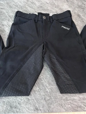 Svarta ridbyxor från Pikeur - Snygga svarta ridbyxor från Pikeur med helskoning i silikon. Byxorna har två framfickor och bälteshällor. Använda men i bra skick. Storlek 152 cl men passar även xxs.