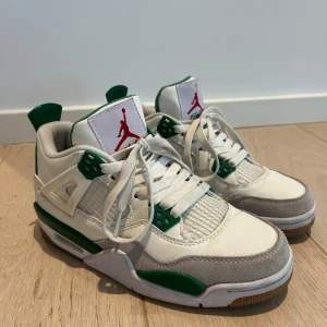 Air Jordan 4 Retro vit/grön - Snygga Air Jordan 4 Retro sneakers i vitt med gröna och grå detaljer. Skorna har meshpaneler, klassisk snörning och Jumpman-logga på plösen. Ovandelen är i läder och mocka, med gummisula för bra grepp. Perfekta för dig som gillar streetwear och sportig stil.