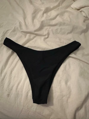 Svarta bikiniunderdelar high cut - Säljer ett par svarta bikiniunderdelar med high cut-modell. De har en enkel och stilren design utan synliga detaljer eller mönster. Perfekta för dig som gillar en klassisk look på stranden eller vid poolen.