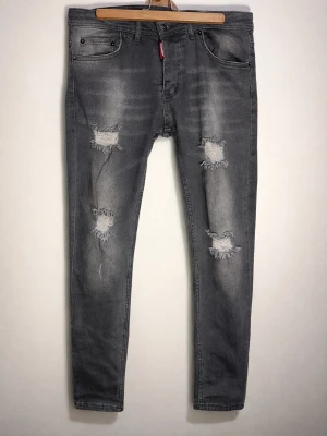 Dsquared2 Grå slitna skinny jeans med hål - Säljer ett par grå skinny jeans med slitningar och hål på både lår och knän. Jeansen har fem fickor och en klassisk knappgylf. Materialet är denim med stretch för skön passform. Perfekta för en avslappnad och trendig look.