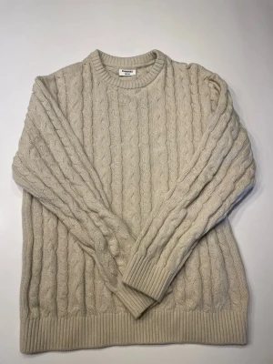 Beige kabelstickad tröja från Kappahl  - Säljer en beige kabelstickad tröja från kappahl med rund halsringning och ribbade muddar vid ärmslut och nederkant. Tröjan har ett klassiskt flätmönster och är perfekt för dig som gillar en stilren och mysig look.