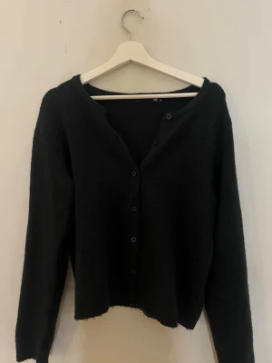 Svart kofta med knappar - Mysig svart kofta med långa ärmar och knäppning framtill. Koftan har en enkel, rak passform och är tillverkad i ett mjukt, fluffigt material. 