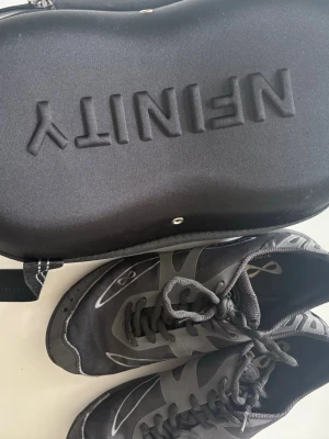 Svarta träningsskor från NFINITY - Säljer ett par svarta träningsskor från NFINITY med grå detaljer och snörning. Skorna har en sportig design med slitstark sula och ventilerande meshmaterial. Perfekta för gymmet eller löpning. Medföljer praktisk förvaringsväska. används främst vid Cheer, Max 9 träningar använd, köpte för 1900