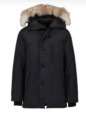 Svart parkas från Canada Goose Äkta - Snygg svart parkas från Canada Goose med avtagbar huva och äkta pälsdetalj. Jackan har stora knappar, dragkedja, flera fickor och klassisk logotyp på ärmen. Perfekt för kalla dagar med sin tjocka vaddering och vindtäta material. Nypris 20 000