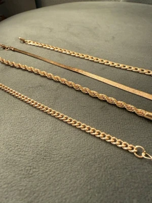 Fyra guldiga armband i olika kedjor - Säljer fyra stilrena armband i guldfärgad metall. Varje armband har unik kedjedesign: pansarkedja, orm-kedja, tvinnad kedja och klassisk länk. Perfekta för att mixa och matcha till din egen stil. Alla har justerbara länkar för flexibel passform.
