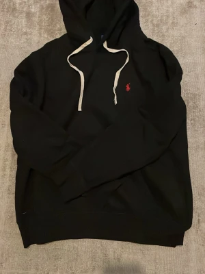 Svart hoodie från Polo Ralph Lauren - Svart hoodie från Polo Ralph Lauren med vit dragsko och den klassiska röda loggan, helt ny skick